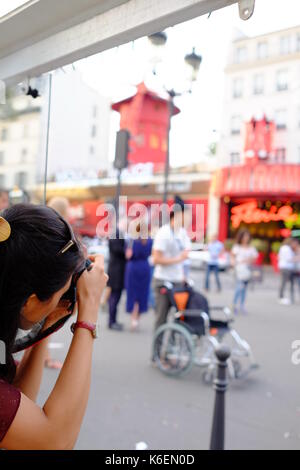 A tourist takes a photo of the crowds outside the Moulin Rouge in Montmartre, Paris Stock Photo
