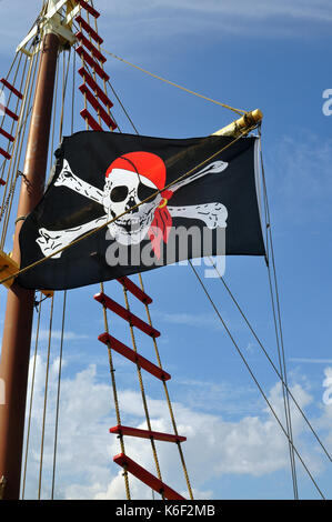 Black, White, and Red Pirate Flag flying on a ship against a blue sky. Stock Photo