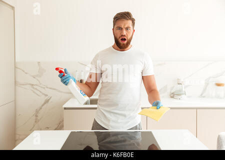 Shocked bearded man with cleaners on kitchen looking at the camera Stock Photo