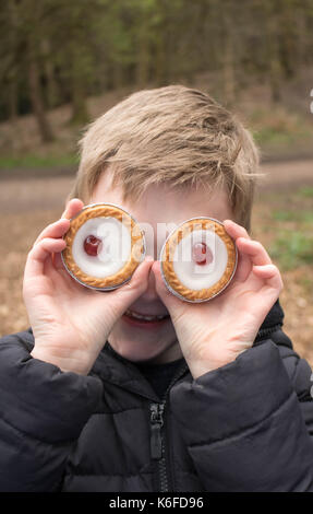 Boy plays with Bakewell Tarts while on picnic pretending that they are eyes Stock Photo