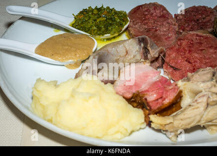 Boiled meat of mixed meat whit potatoes and green sauce and spicy sauce in a white porcelain dish Stock Photo