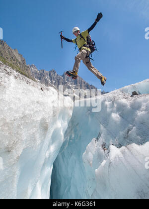 Mountain climber jumping over crevasse on Mer de Glace glacier, Mont Blanc massif, Chamonix, Haute-Savoie, France Stock Photo