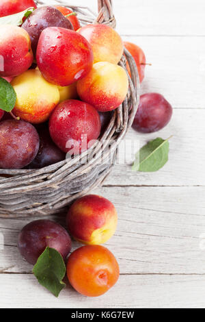 Fresh ripe peaches and plums in basket on wooden table Stock Photo