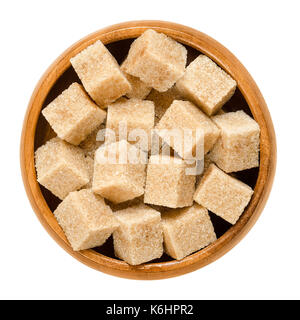 Demerara brown sugar cubes in wooden bowl. Also called sugar lumbs. Sucrose sugar product with distinctive brown color. Macro photo. Stock Photo