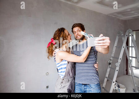 Couple at home painting walls, taking selfie with smartphone. Stock Photo