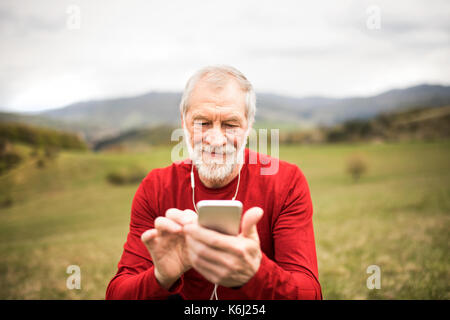 Senior runner in nature with smartphone and earphones. Stock Photo