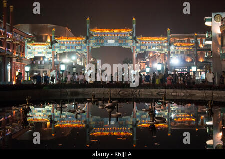 Crowds of pedestrians walk through the traditional Chinese Paifang gateway at the entrance to Qianmen Street, reflected in the waters of a fountain at Stock Photo