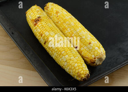 Two ears of blackened roasted corn on baking sheet Stock Photo