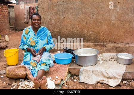 A middle-aged black Ugandan woman sitting and preparing food for cooking in front of her house. Stock Photo
