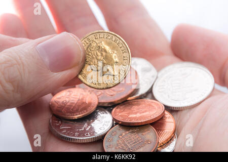 An old 2015 pound coin being picked up from a handful of assorted coins Stock Photo