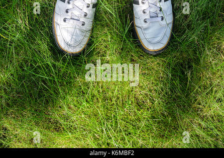 White sneakers on a green grass top view. A view from the first person under the feet to the fresh green grass. Walking on the grass concept Stock Photo