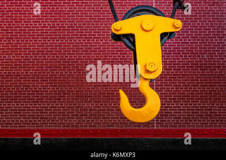 Industrial Hook - Bright yellow crane hook against a red brick wall. Stock Photo