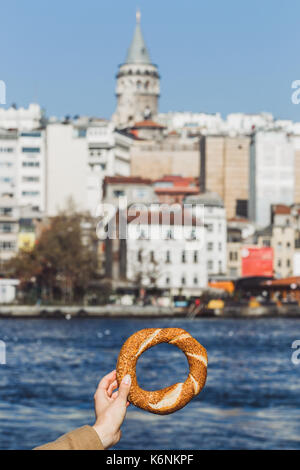 Woman hand holding a traditional Turkish simit on sea background and Galata Tower