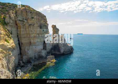 Maltese cliff, showing cliff erosion: wave cut platform, sea cave and stacks. Evidence of cliff recession. A merchant ship on the horizon and a yacht. Stock Photo