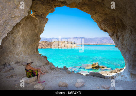 Amazing summer view of woman in a cave at Koufonisi island with magical turquoise waters, lagoons, tropical beaches of pure white sand. Stock Photo