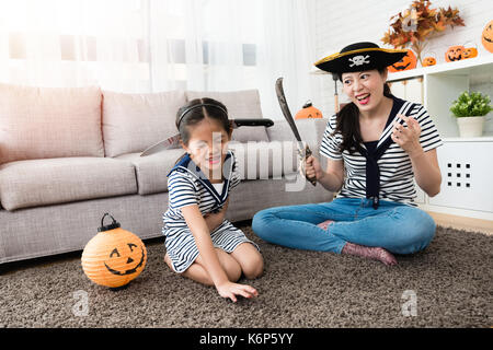 horror pirate mother play the killing game with her cute girl and put the knife on her head for Halloween holiday in the living room Stock Photo