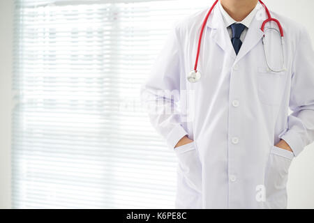 Unknown doctor posing two hand in pocket in the office, he is wearing a stethoscope . Stock Photo
