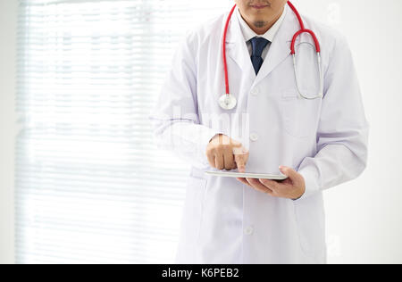 Unknown doctor posing using digital table with bright background, he is wearing a stethoscope . digital table in the office, he is wearing a stethosco Stock Photo