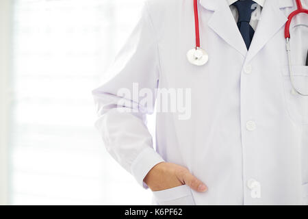 Unknown doctor posing  hand in pocket in the office, he is wearing a stethoscope . Stock Photo
