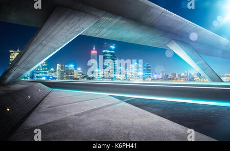 Empty asphalt road under the bridge during the night with beautiful city skyline background . Stock Photo