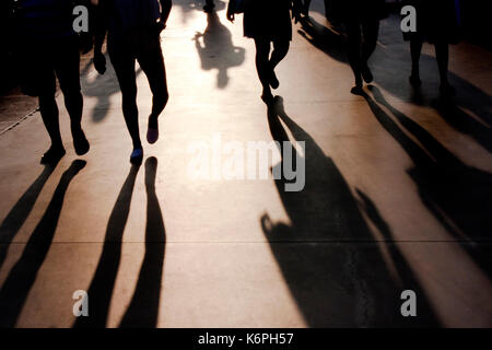 Blurry shadows of people walking towards the camera on seaside promenade in misty summer sunset Stock Photo