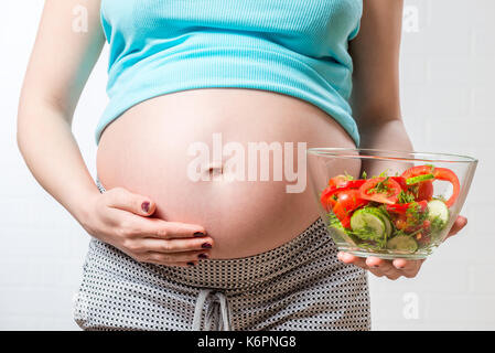belly of a pregnant woman and a bowl of vegetable salad close-up Stock Photo