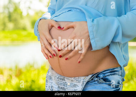 Belly of a pregnant woman close-up, hands in the shape of a heart on the stomach Stock Photo