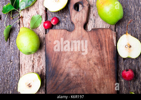Pear and small apple around empty cutting board on wooden rustic background. Top view. Frame. Autumn harvest. Copy space Stock Photo