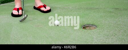 Playing mini golf. Low angle closeup view of mini golf ball and golf club near hole. Stock Photo