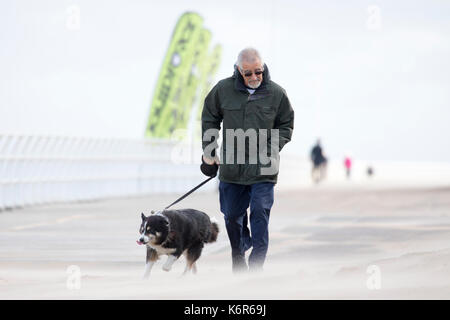 North Wales, UK Weather. The first named storm of season that brought 75mph gales to a central belt of the UK and North Wales now passing over North East of the UK. The Amber Warning for wind and rain is now reduce to yellow warning over North Wales as this dog walker discovered along the promenade with the blowing sands in Rhyl this morning, Denbighshire, Wales as this man discovered grimacing from the drifting sands Stock Photo