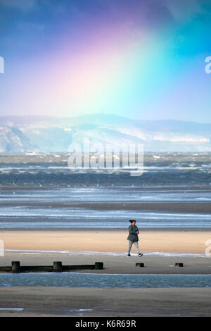North Wales, 13th September 2017.  UK Weather. The first named storm of season that brought 75mph gales to a central belt of the UK and North Wales now passing over North East of the UK. The Amber Warning for wind and rain is now reduce to yellow warning over North Wales as this person discovered walking along the the beach in Rhyl this morning, Denbighshire, Wales as this lone waman walks along the beach at Rhyl with a glorious rainbow in the distance over Llandduno Stock Photo