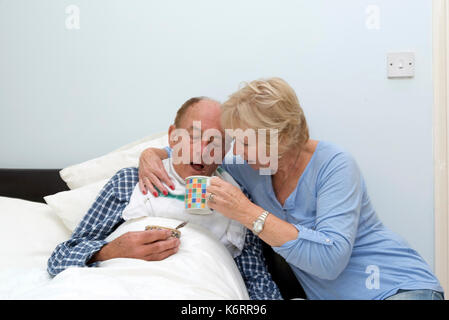 Elderly bedridden man being given a drink by his carer and wife Stock ...