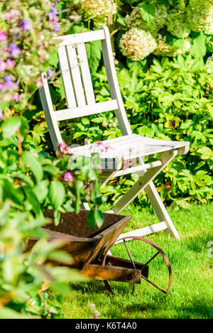 Still life of outdoor chair and wheelbarrow in garden. Stock Photo