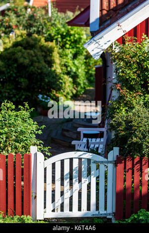 Small white garden gate sided by red picket fence. Stock Photo