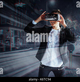 Young girl getting experience VR headset, is using augmented reality eyeglasses, being in a virtual reality. In city at night. Stock Photo