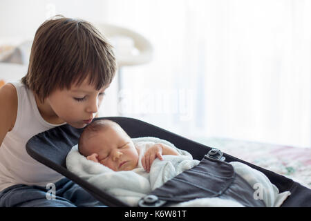 Beautiful boy, hugging with tenderness and care his newborn baby brother at home. Family love happiness concept Stock Photo