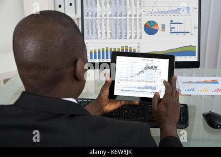 Rear View Of Young African Businessman Analyzing Graph On Digital Tablet In Office Stock Photo
