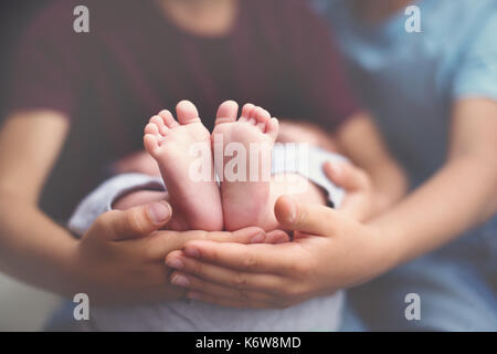 Little baby feet in brothers hands, two children holding their baby brothers feet in hands