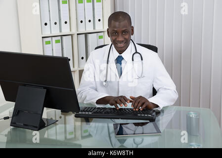 Young Happy African Doctor Working On Computer At Desk Stock Photo