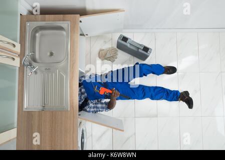 High Angle View Of Handyman Lying On Floor Repair Sink In Kitchen Stock Photo