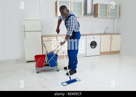 African Male Worker In Overall Cleaning Floor With Mop Stock Photo