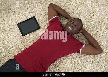High Angle View Of Smiling Man With Digital Tablet Lying On Carpet Stock Photo