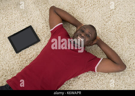 High Angle View Of Smiling Man With Digital Tablet Lying On Carpet Stock Photo