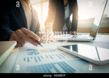Business team two colleagues discussing new plan financial graph data on office table with laptop and digital tablet. Stock Photo