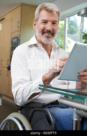 Portrait Of Disabled Man In Wheelchair Using Digital Tablet At Home Stock Photo