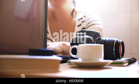 Freelance professional photographer woman working from home with a computer and a camera. Cup of coffee and notebook on the desk. Empty copy space for Stock Photo