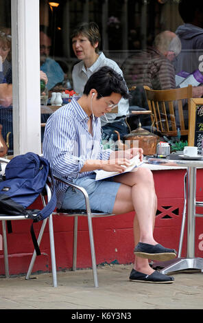 young male person sitting outside cafe reading book, cambridge, england Stock Photo
