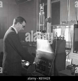 1950s, historical, man in a pinstripe suit using a machine on a work bench to do experiments on the spinning of rayon fibers, England, UK. Stock Photo