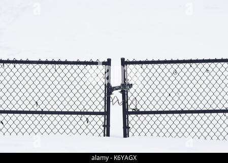 Closed and locked chain link fence gate on a snowy driveway in Speculator, New York NY USA Stock Photo