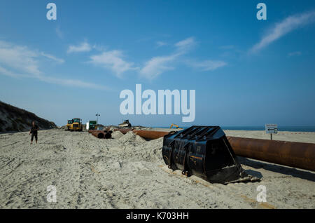 Am Strand, Langeoog.  Deutschland.  Germany.  A close-up of the industrial pipeline used as part of the active beach rebuilding, Strandaufschüttung, pumping sand up onto the sandy beaches.  Diggers and machinery used to lay the industrial pipeline along the beaches of Langeoog.  It's a sunny day with blue skies and only a few light clouds. Stock Photo